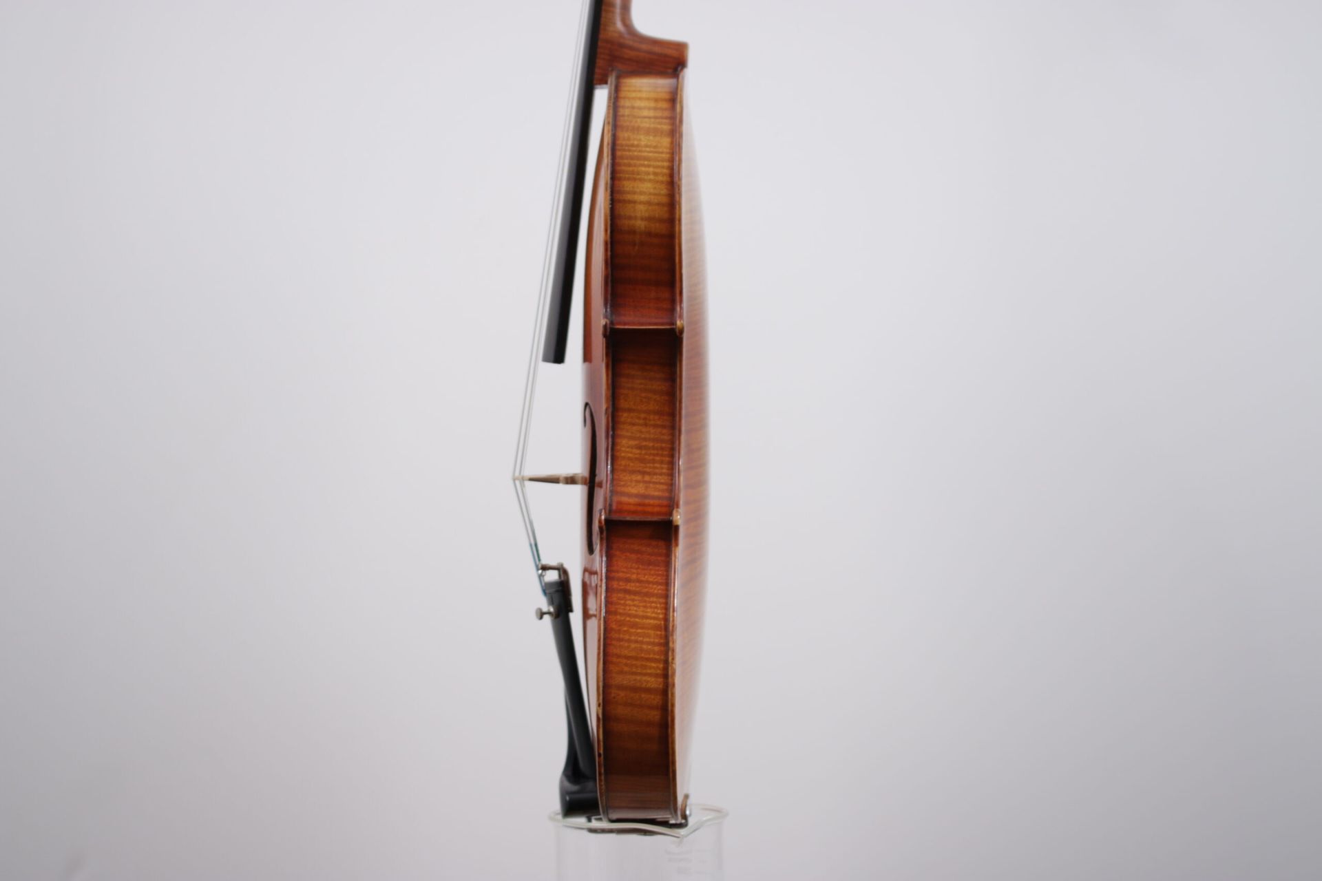 A violin is sitting on a glass stand on a white background.