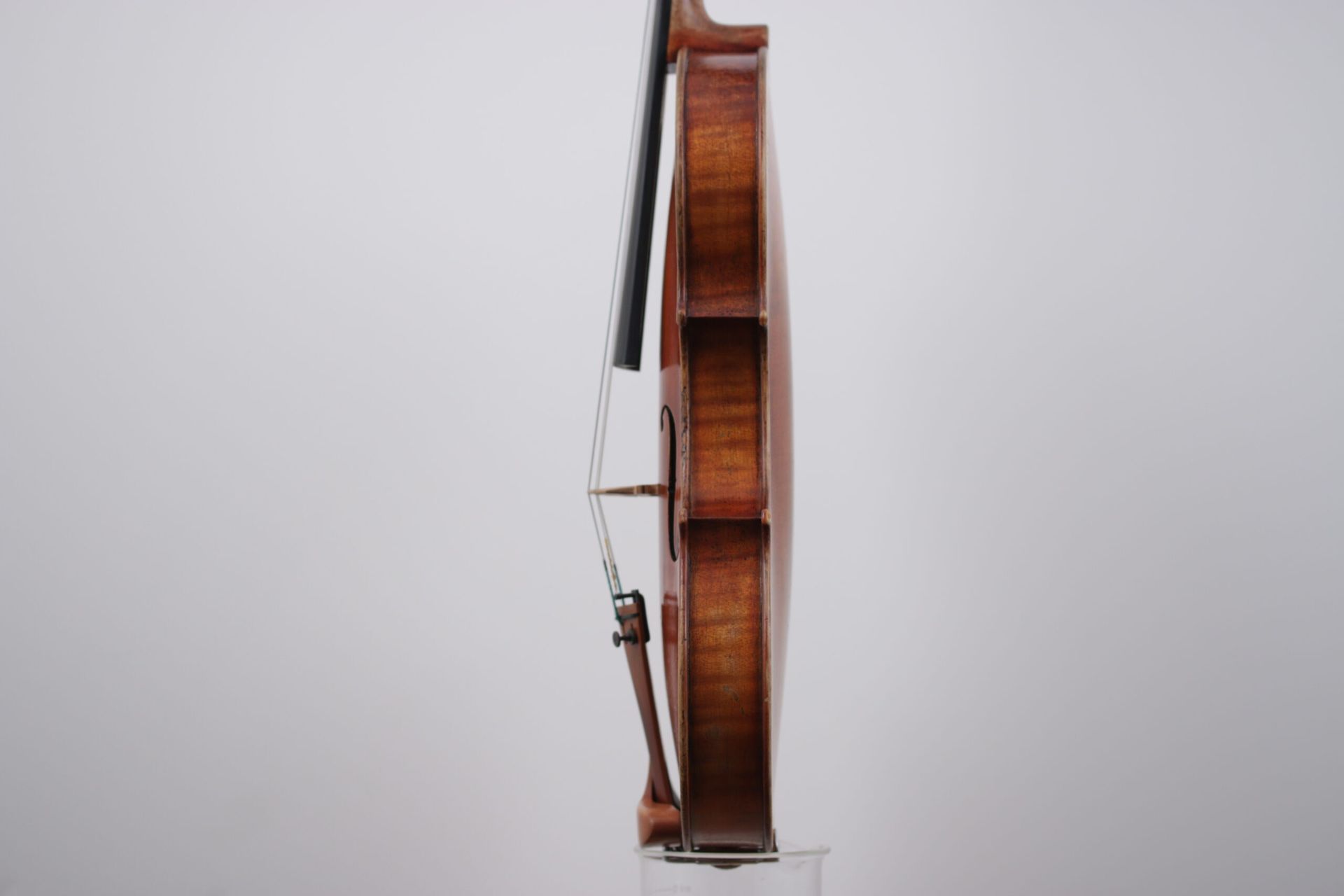 A violin is sitting on a glass stand on a white background.