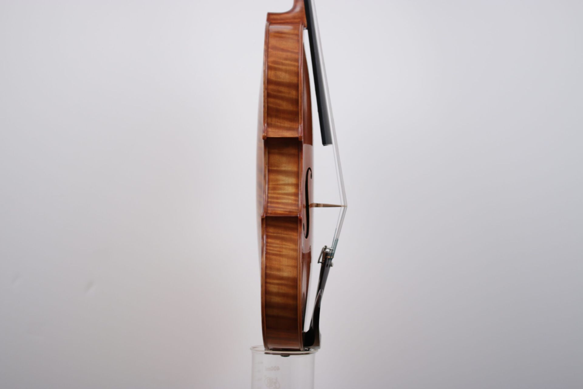 A violin is sitting on a clear stand on a white background.