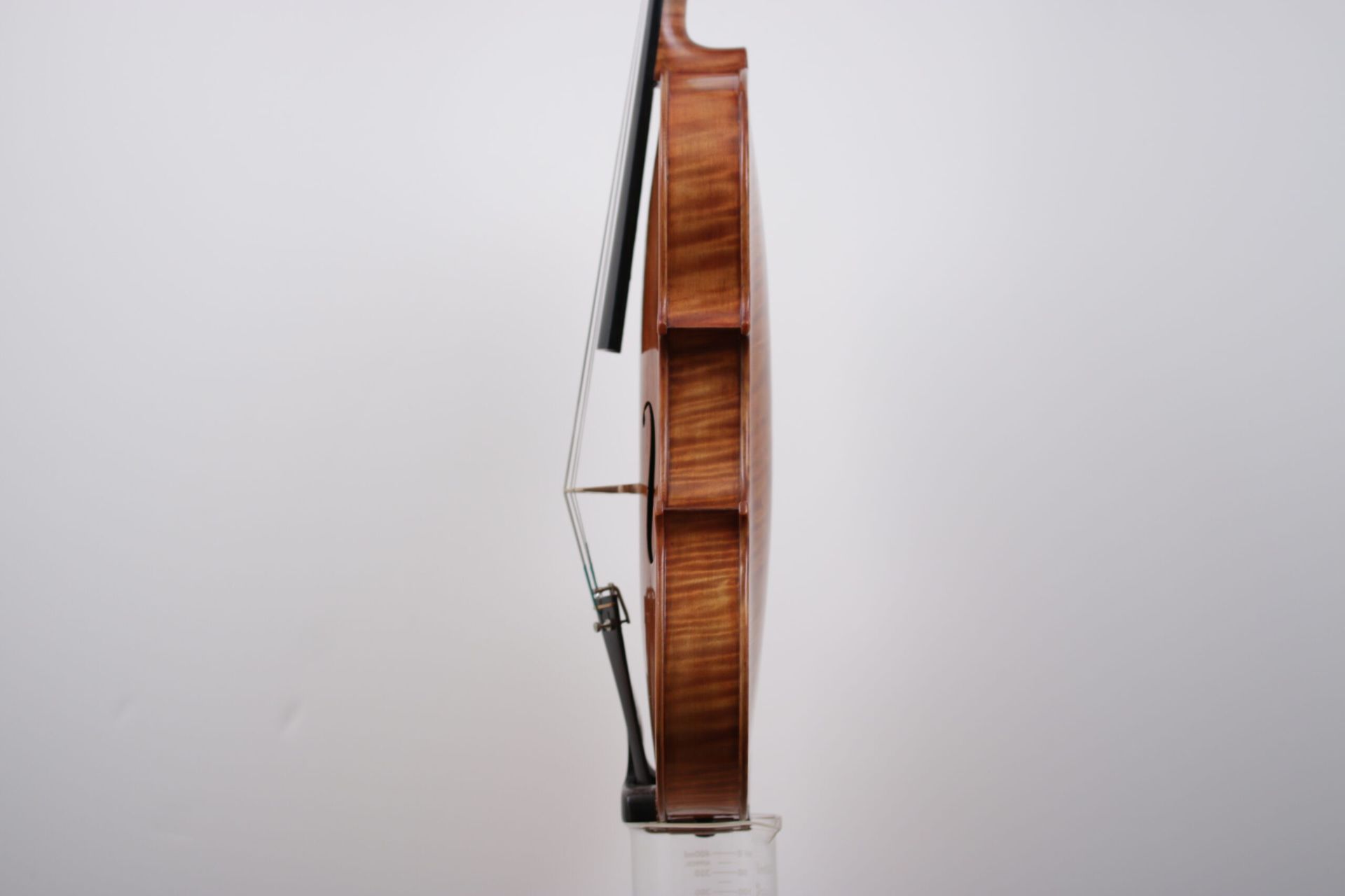 A violin is sitting on a glass against a white wall.