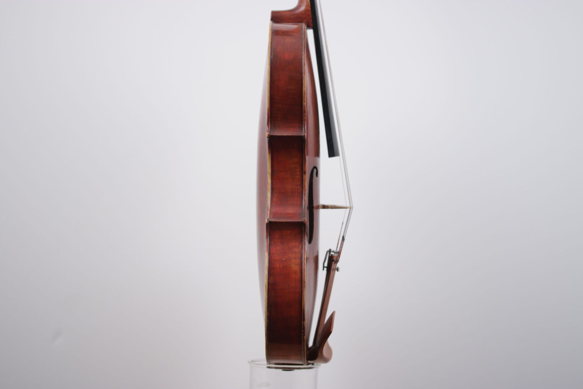 A violin is sitting on a glass stand on a white background.