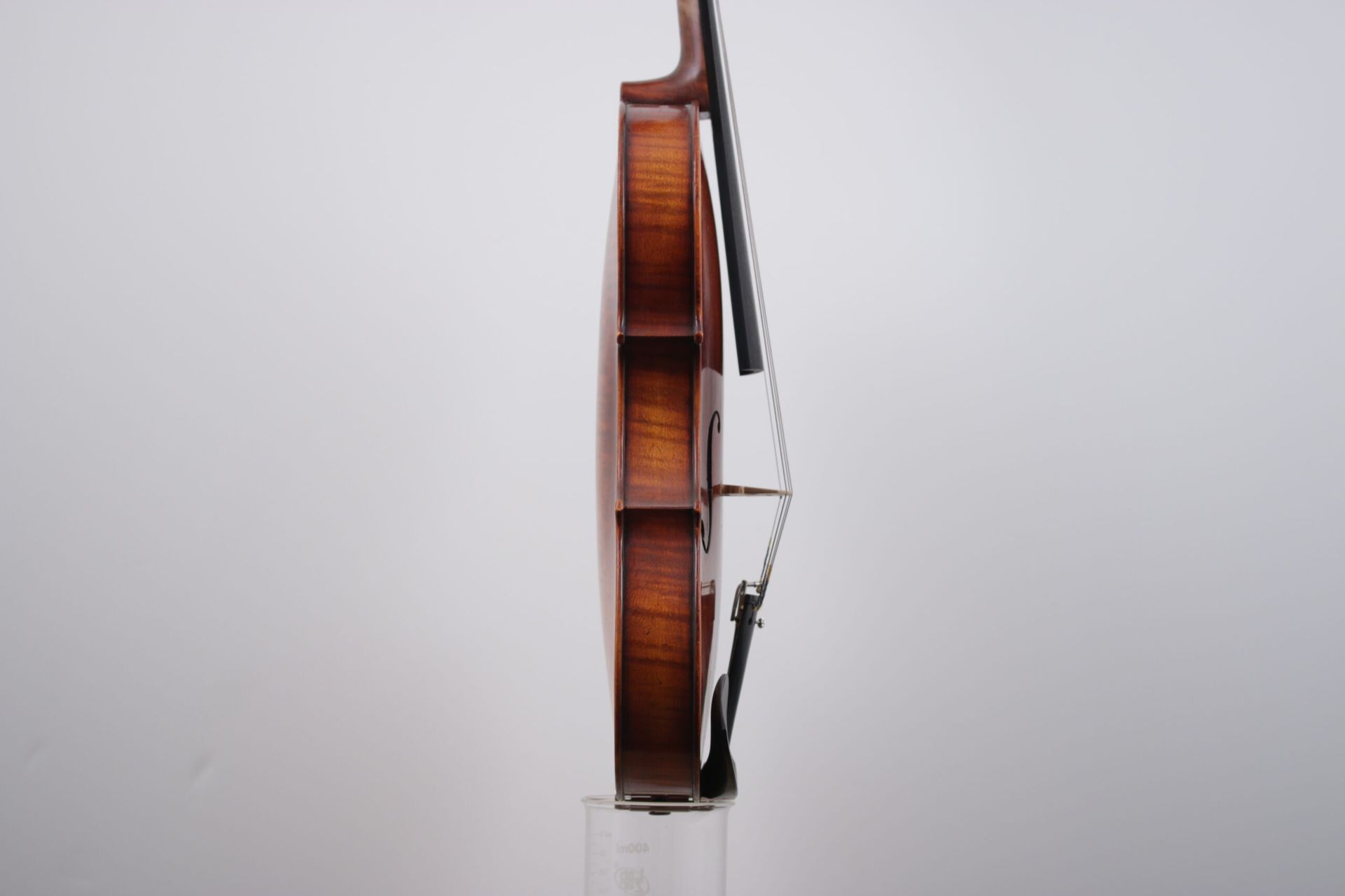 A violin is sitting on a clear stand on a white background.