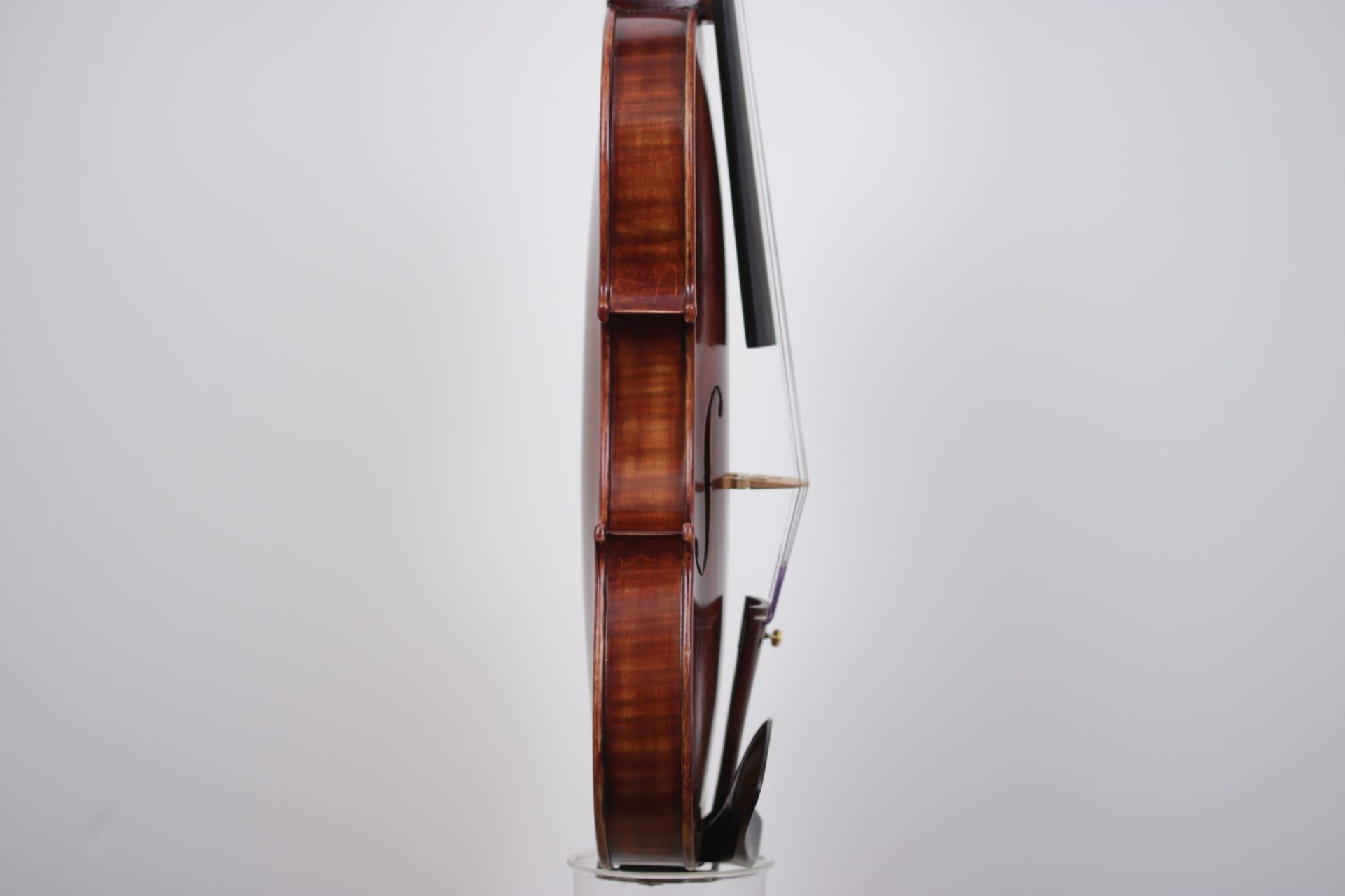 A violin is sitting on a glass stand on a white background.