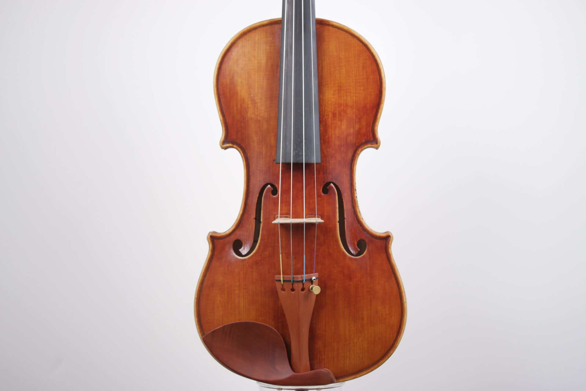 A violin is sitting on a stand on a white background.
