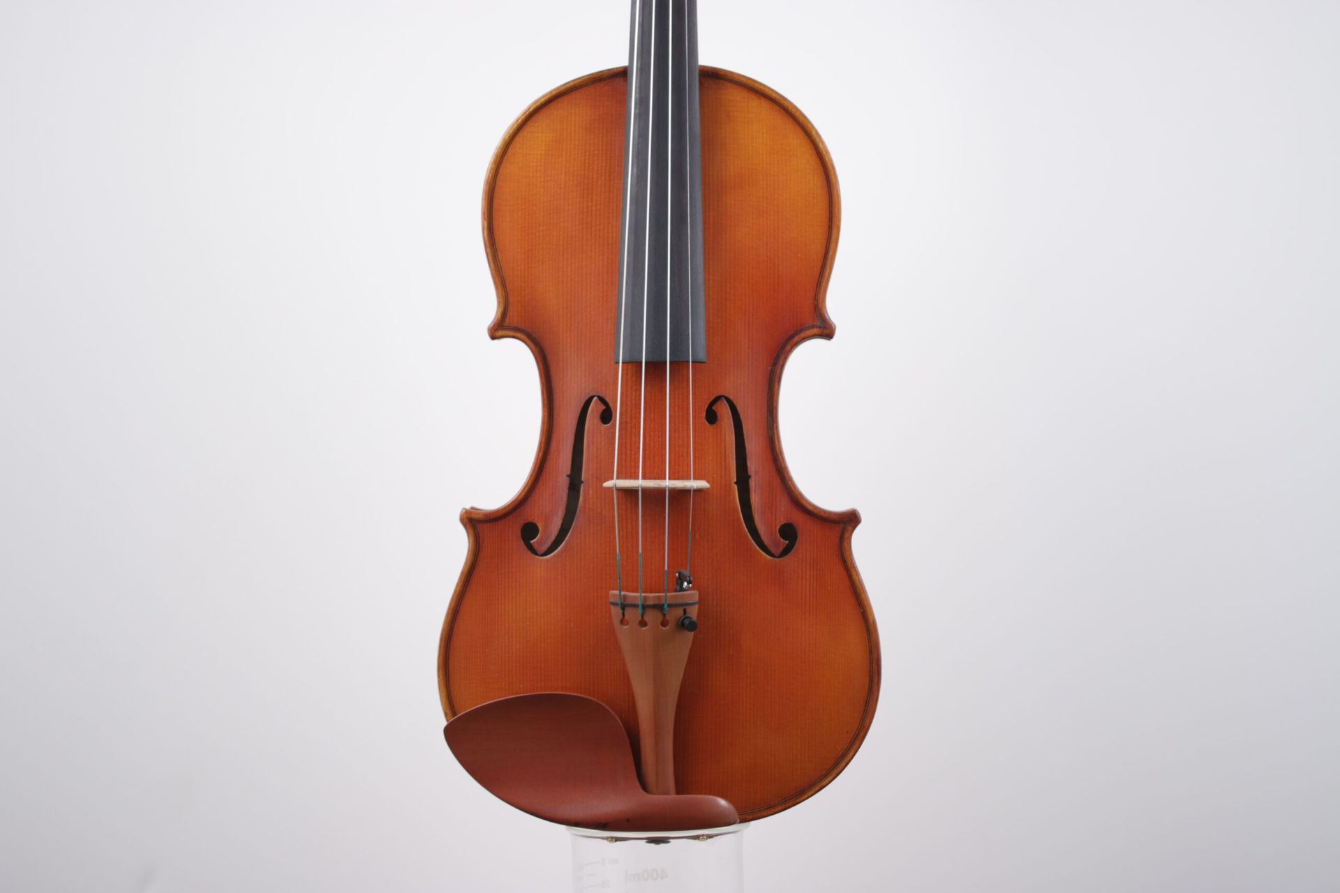 A violin is sitting on a glass stand on a white background