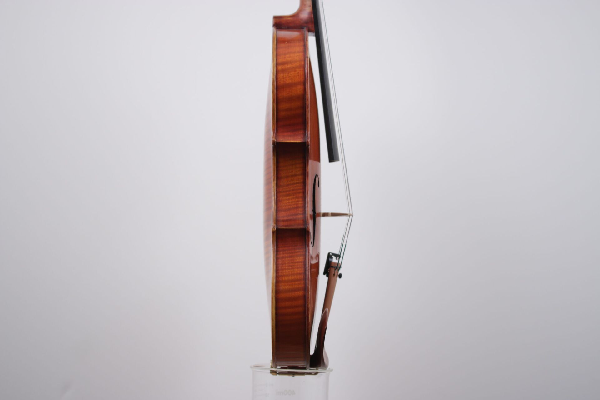 A violin is sitting on a clear display stand on a white background.