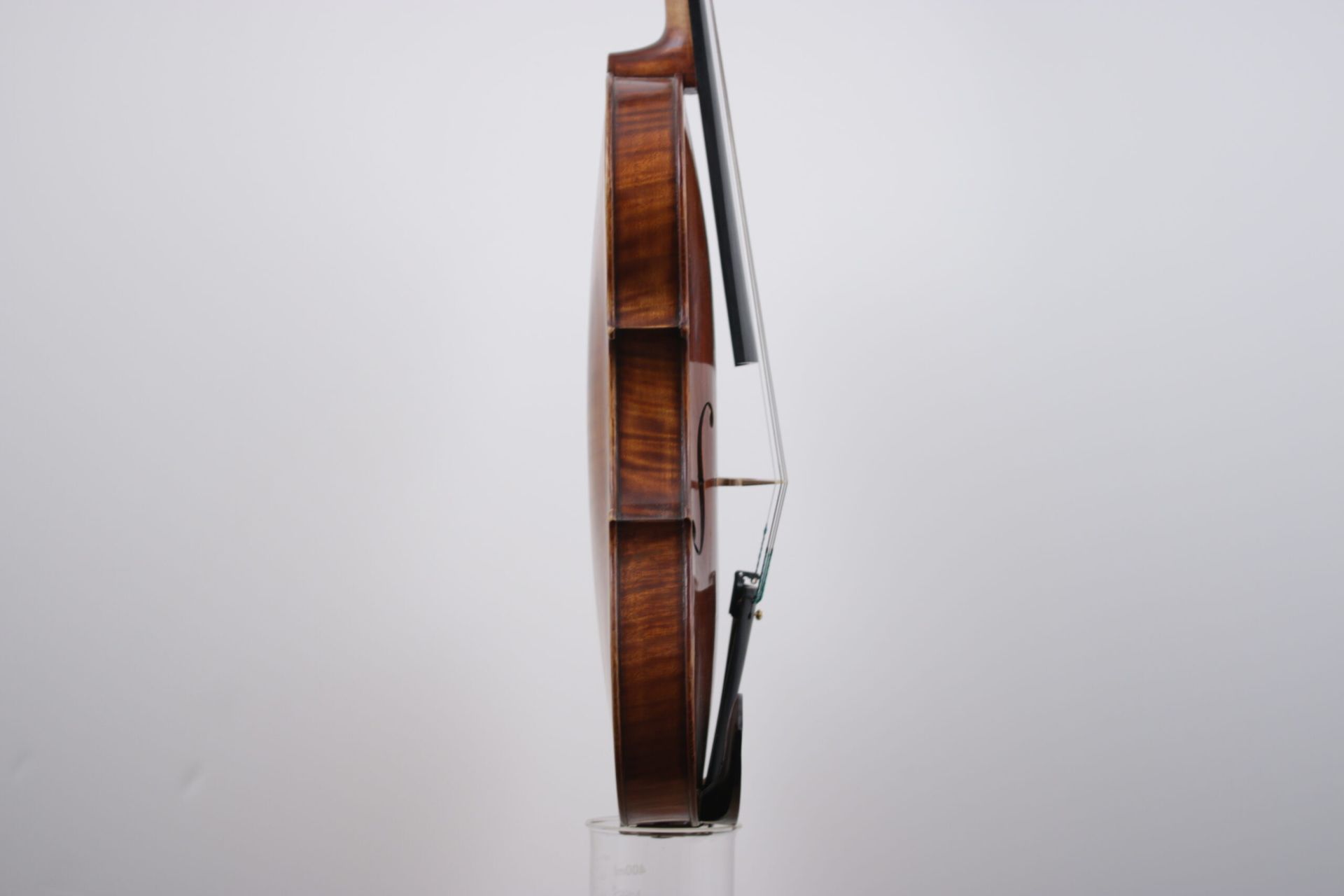 A violin is sitting on a glass stand on a white background.