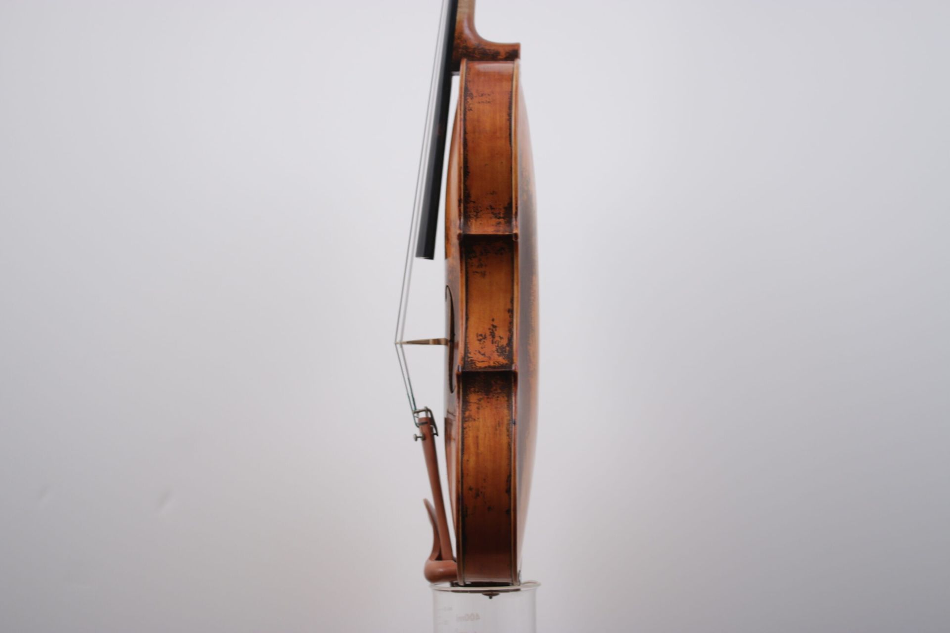 A violin is sitting on a glass stand on a white background.
