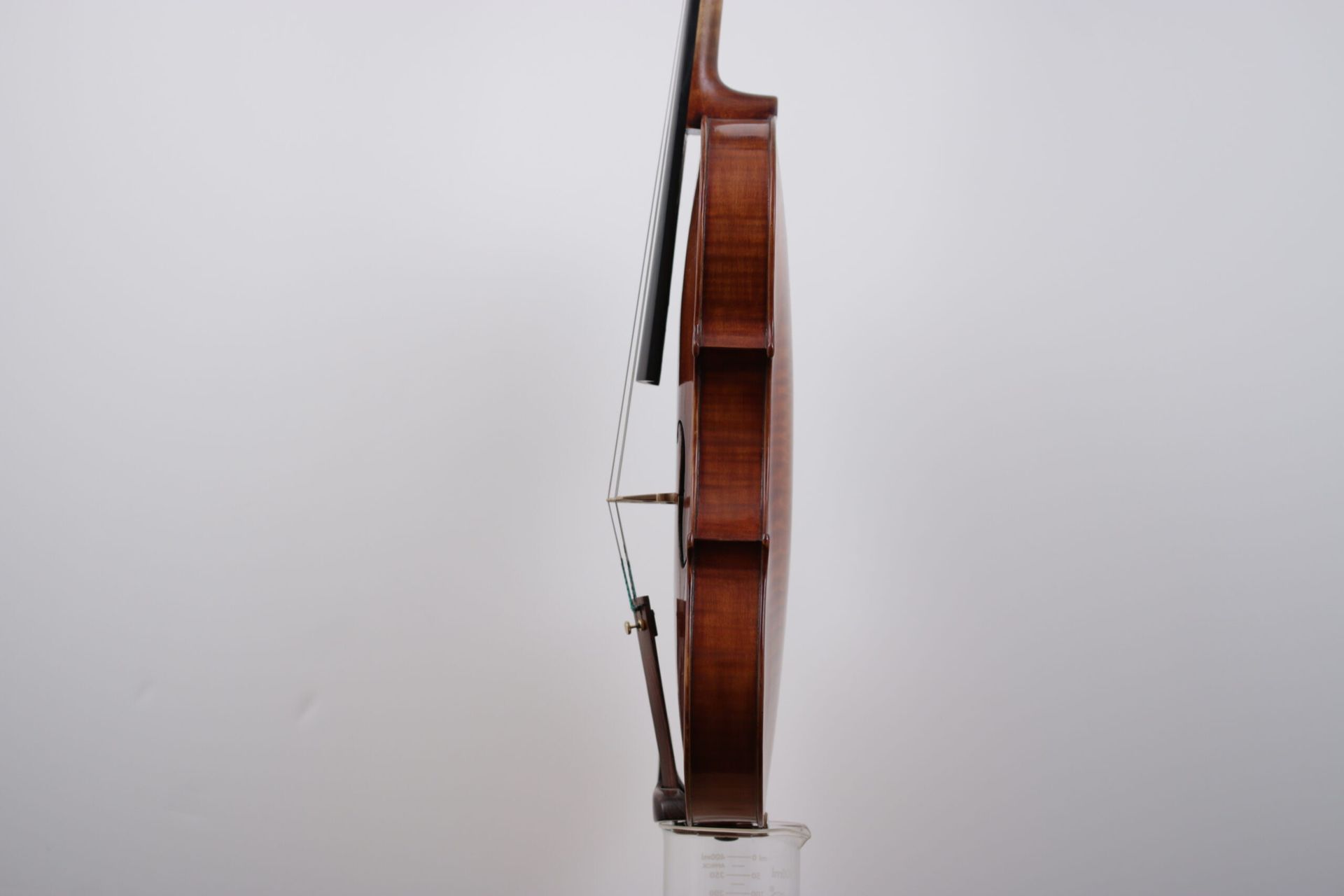 A violin is sitting on a glass stand on a white background.