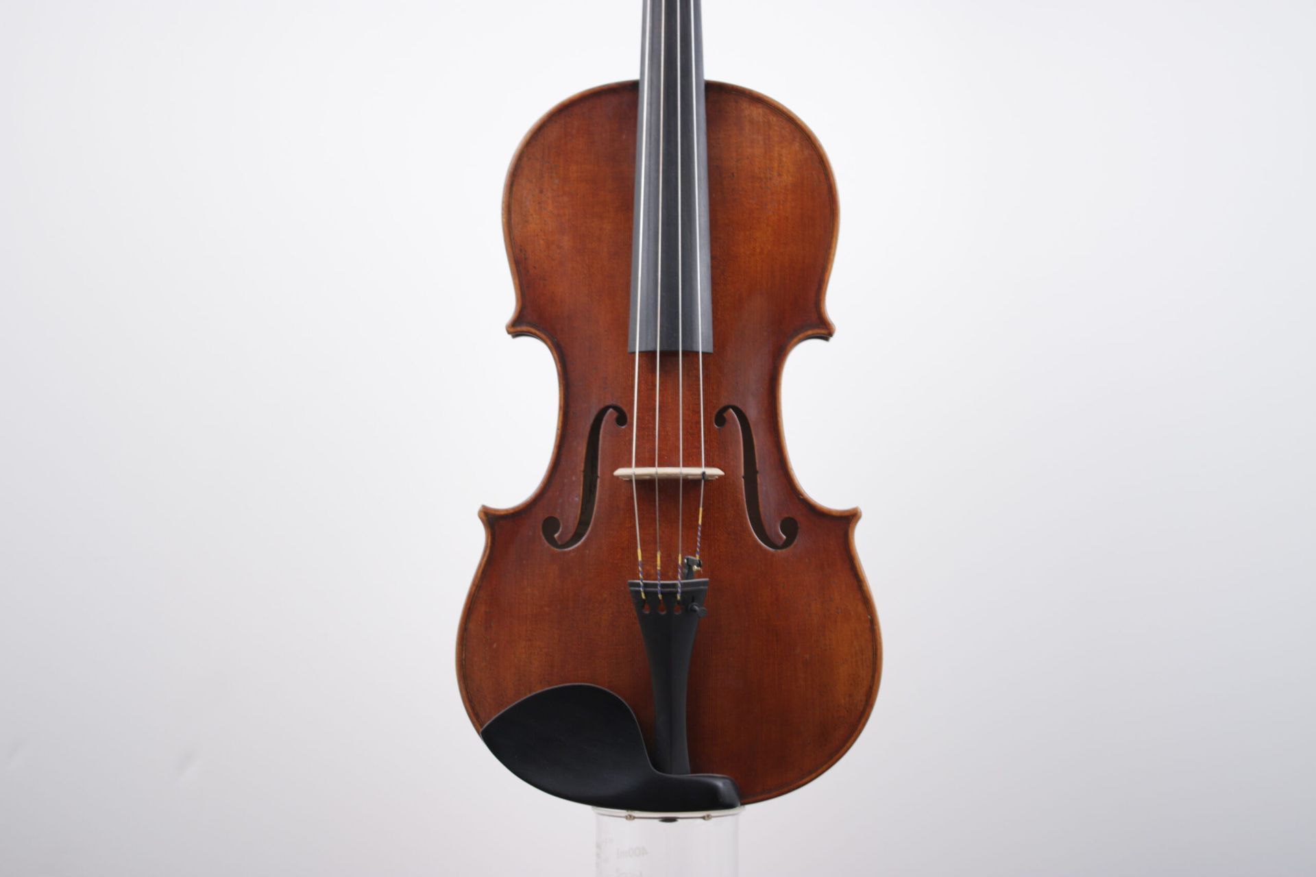 A violin is sitting on a clear stand on a white background.