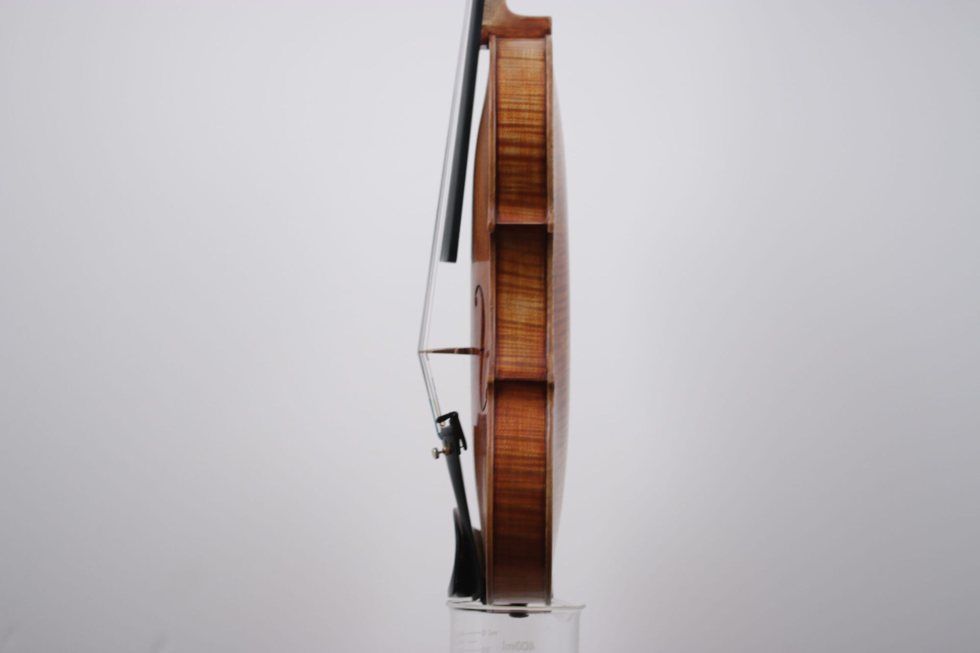 A violin is sitting on top of a clear glass on a white background.