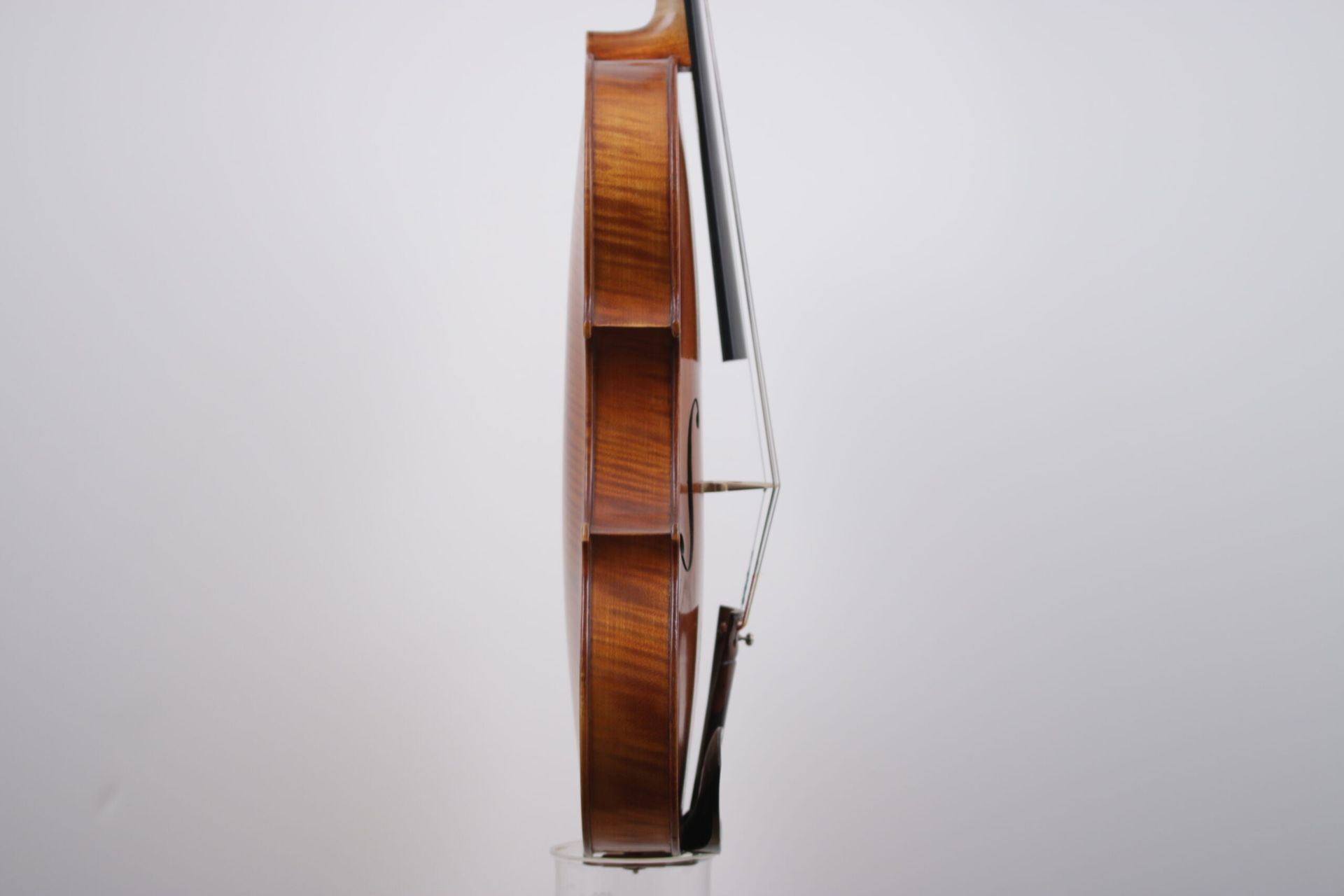 A violin is sitting on a glass stand on a white background.