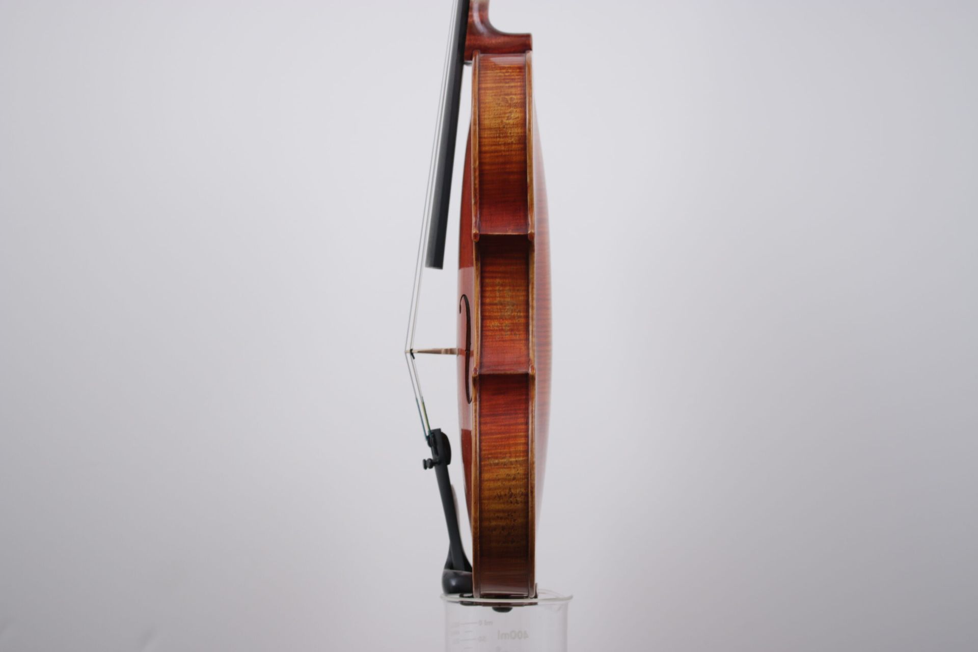 A violin is sitting on top of a glass against a white wall.