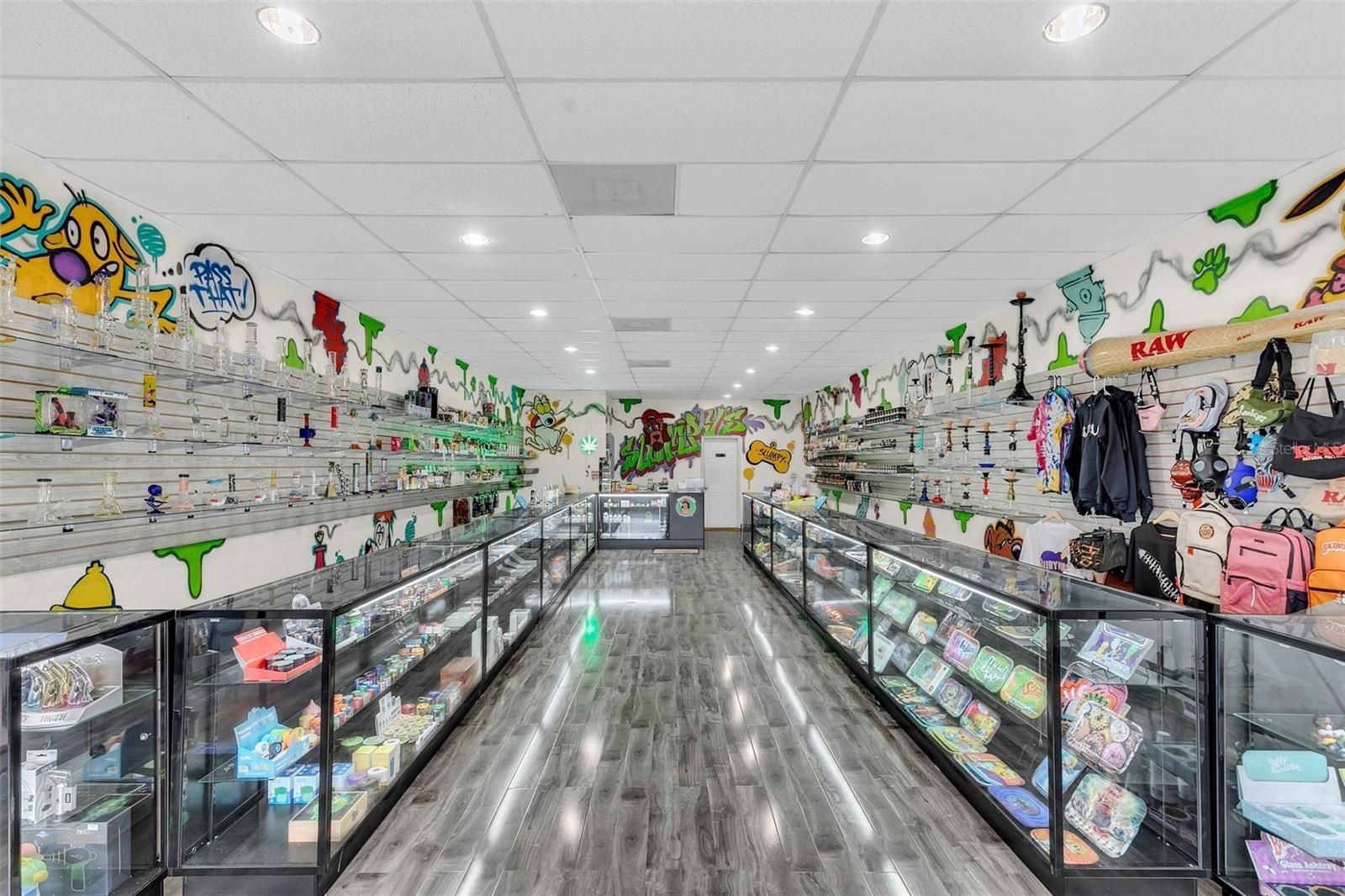 Inside a colorful retail store: long rows of glass display cases, shelves with merchandise, and graffiti-covered walls.