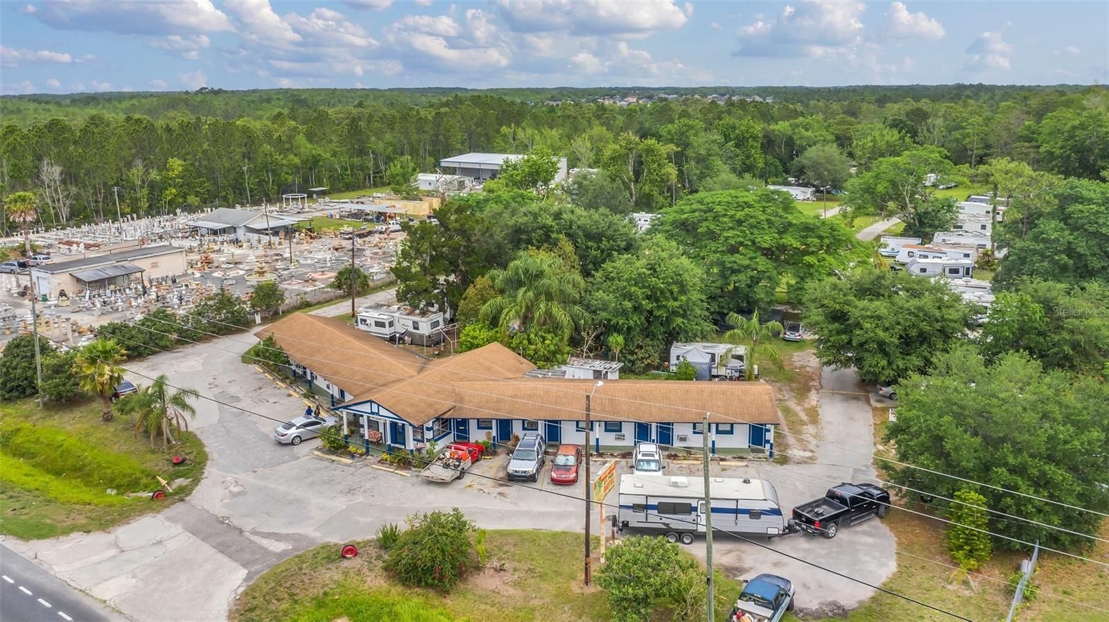 Aerial view of a motel with RVs parked around it. Lush green trees surround the property; a graveyard is visible to the left.