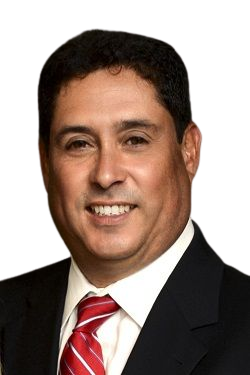Man in a suit and tie smiling at the camera. He has dark hair, a red and white striped tie, and a neutral background.