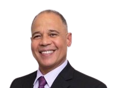 Smiling, middle-aged man with a shaved head, wearing a black suit, purple tie, and light purple collared shirt.