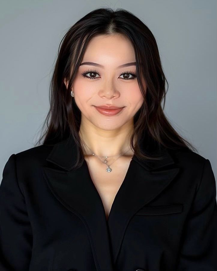 Woman with long dark hair in a black blazer, smiling at the camera. She is wearing light makeup and a silver necklace.