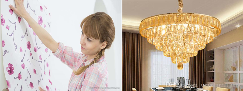 A woman is hanging wallpaper on a wall next to a chandelier.