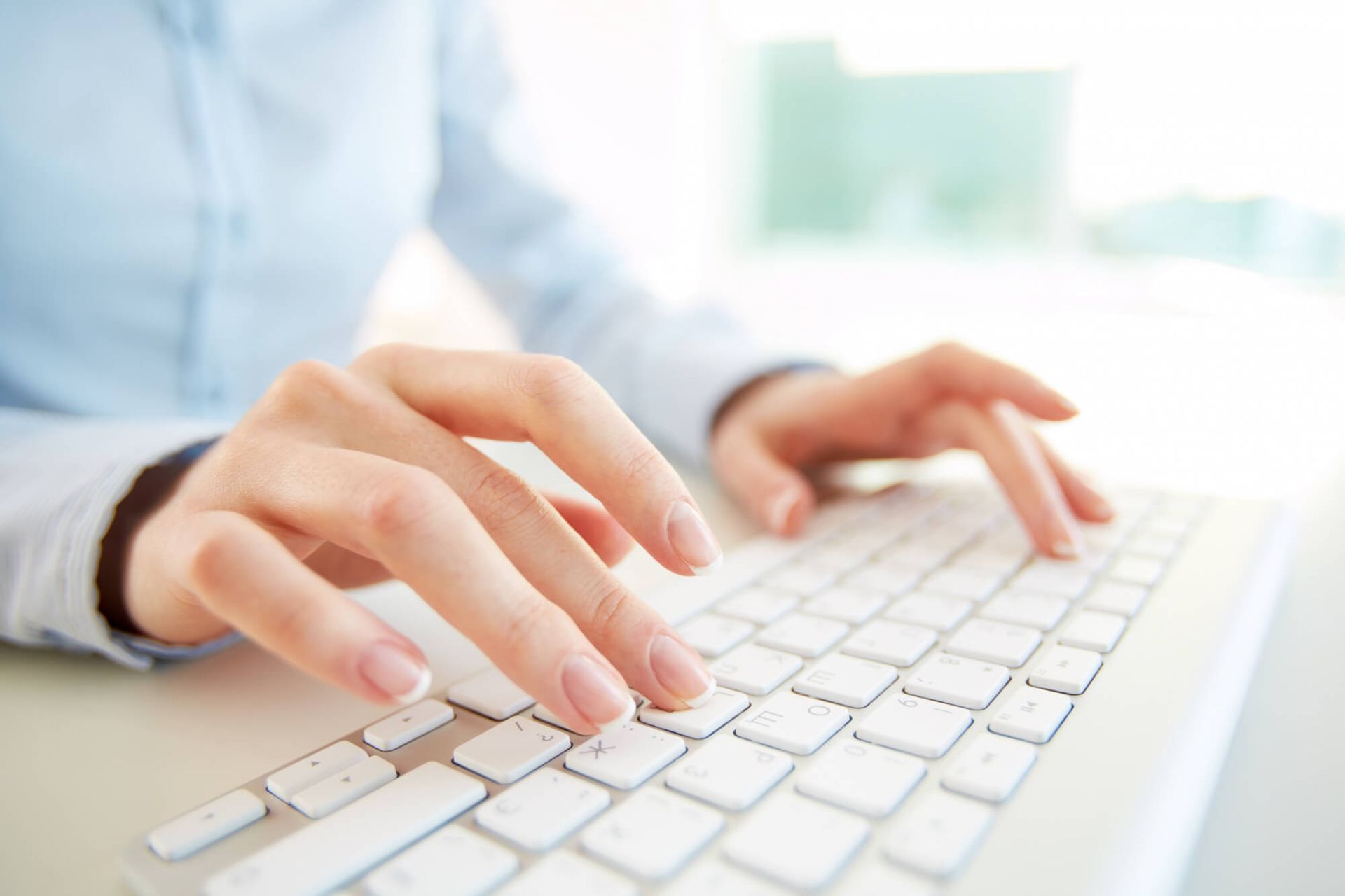 Una mujer está escribiendo en un teclado blanco.