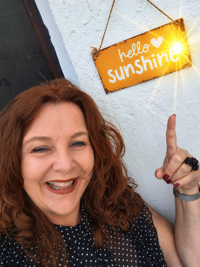 lachende vrouw wijst naar bordje op de muur met de tekst hello sunshine