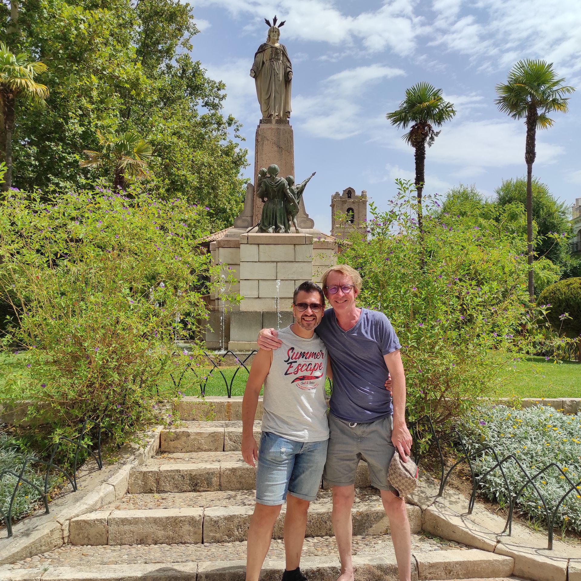 Twee mensen staan ​​op stenen trappen in een park met een monument op de achtergrond.