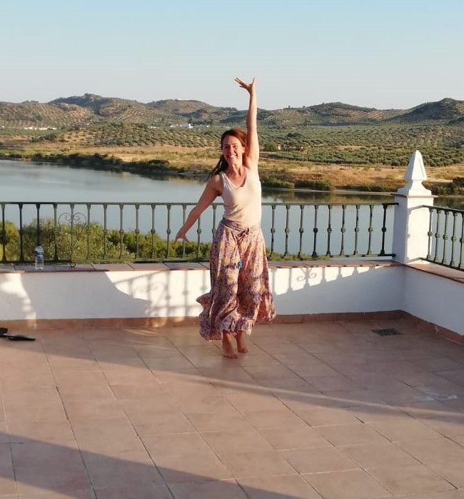 vrouw op terras in Spanje met een rok en een topje aan, dansend met een arme in de lucht
