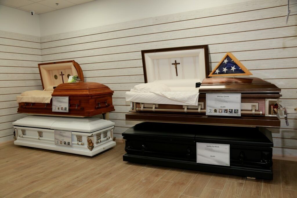 Display of two open caskets in a showroom, one white and one black, with small plaques on top.