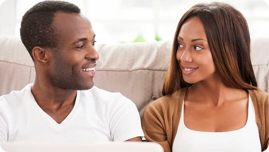 Two people smiling at each other on a couch in a bright living room
