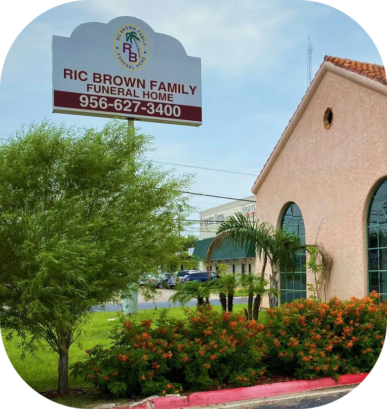 Ric Brown Family Funeral Home sign beside a stucco building and green landscaping