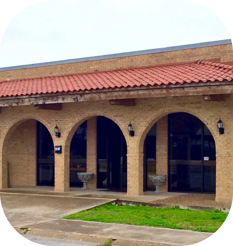 Spanish-style brick building with arched blue-tinted windows, red tile roof, and a concrete walkway in front