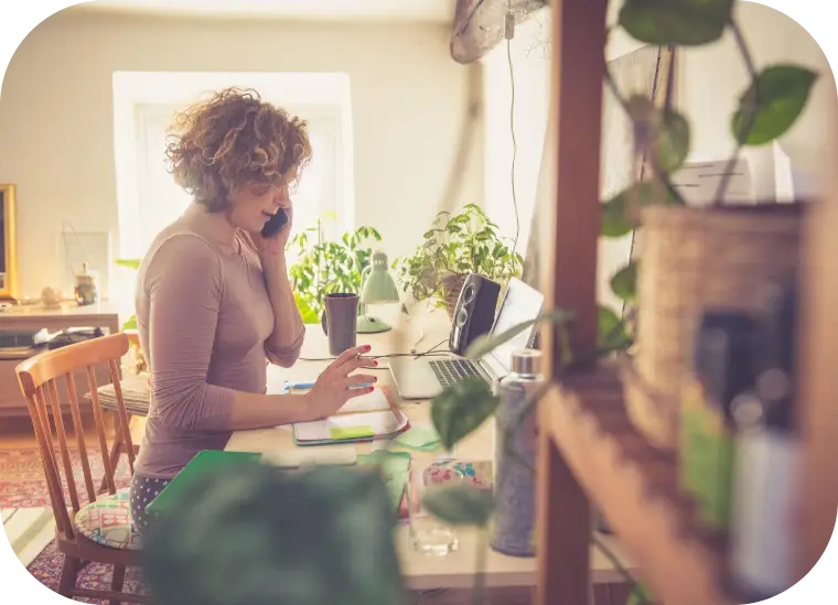 Person working on a laptop at a sunlit kitchen table with plants nearby