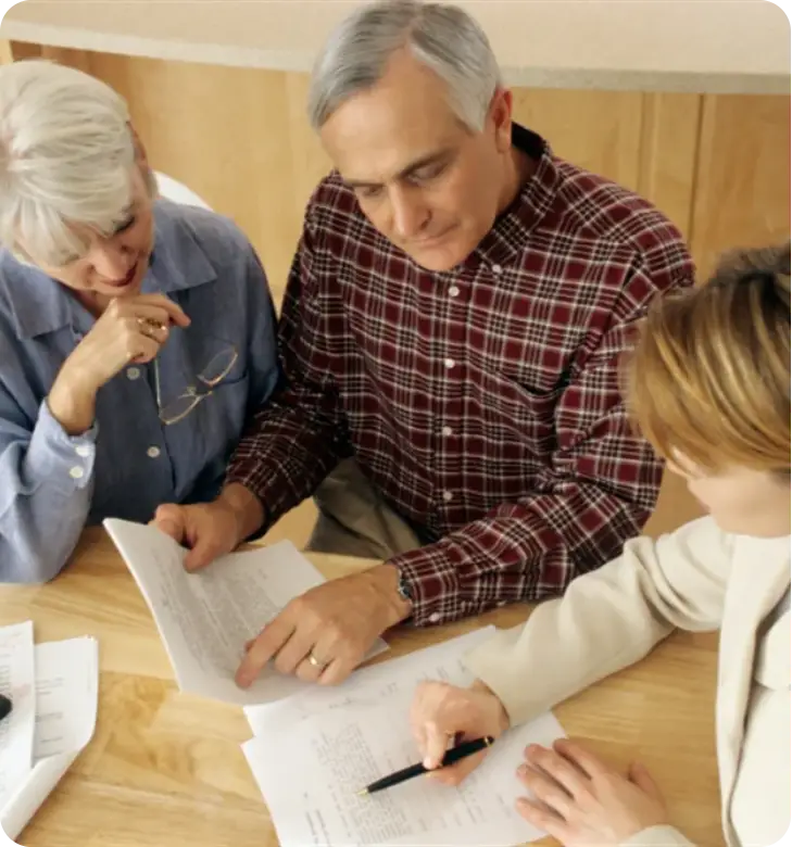 Three people review papers and take notes at a table in a meeting.