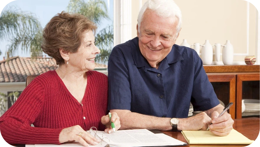 Two adults smiling and writing together at a table by a bright window