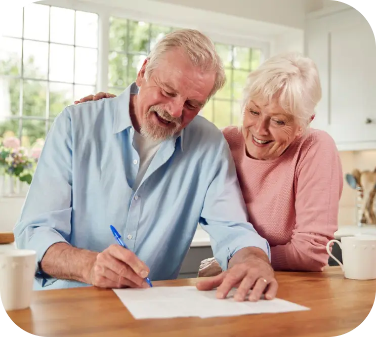 Smiling couple signs a document at a wooden table in a bright kitchen