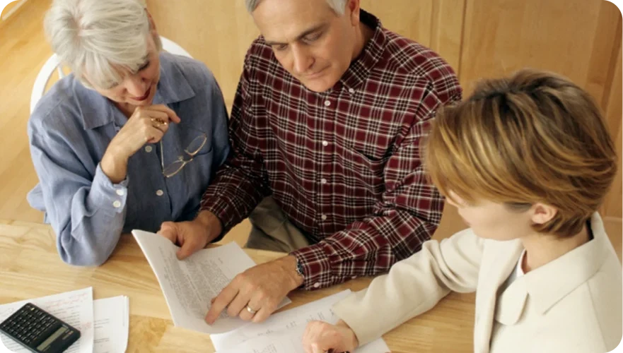 Three people reviewing documents at a wooden table in a bright office