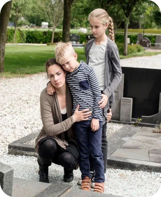 Two adults and a child posing outdoors in a park, with one adult crouching beside them.