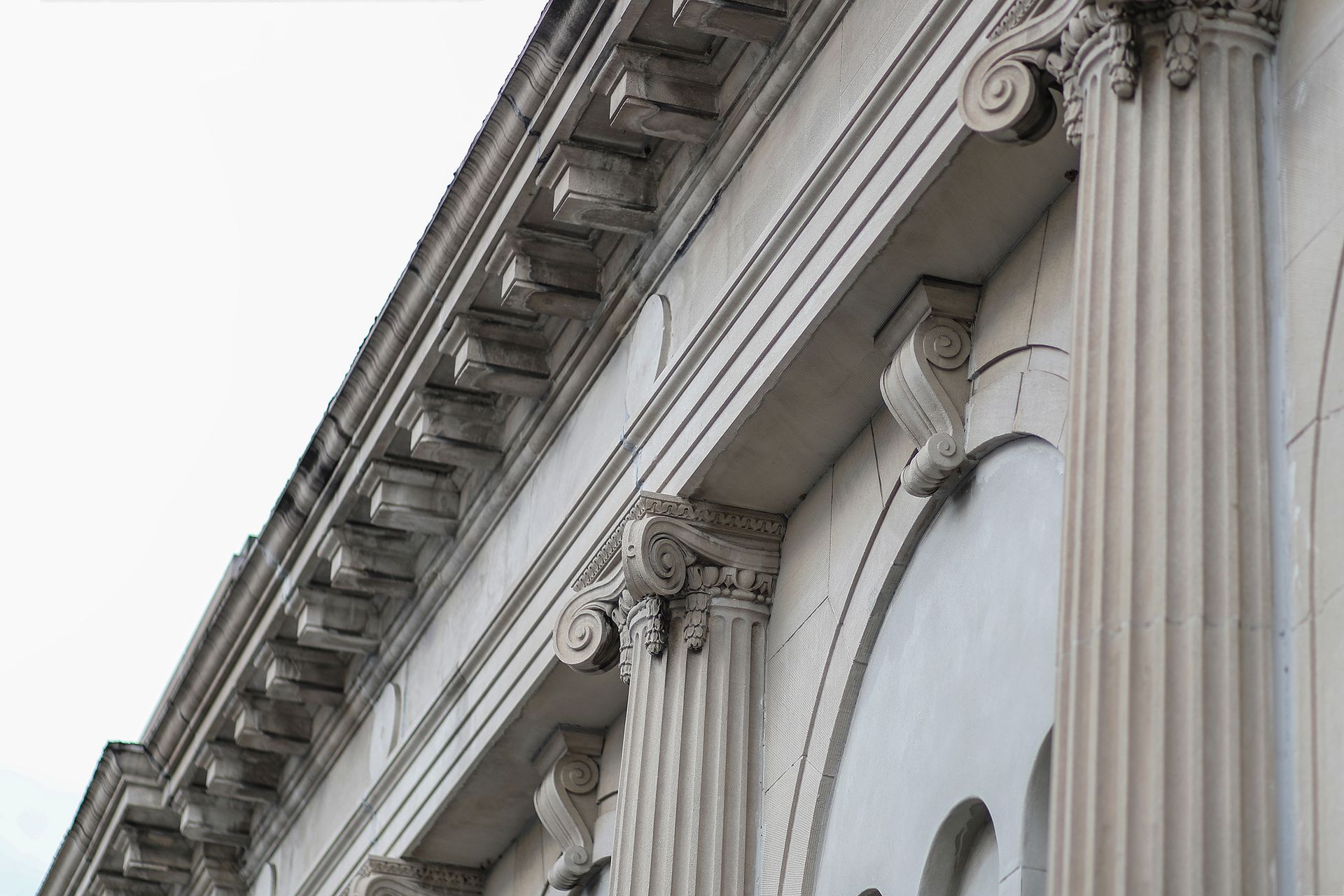 Close-up of ornate stone building facade with columns and arched windows against a pale sky