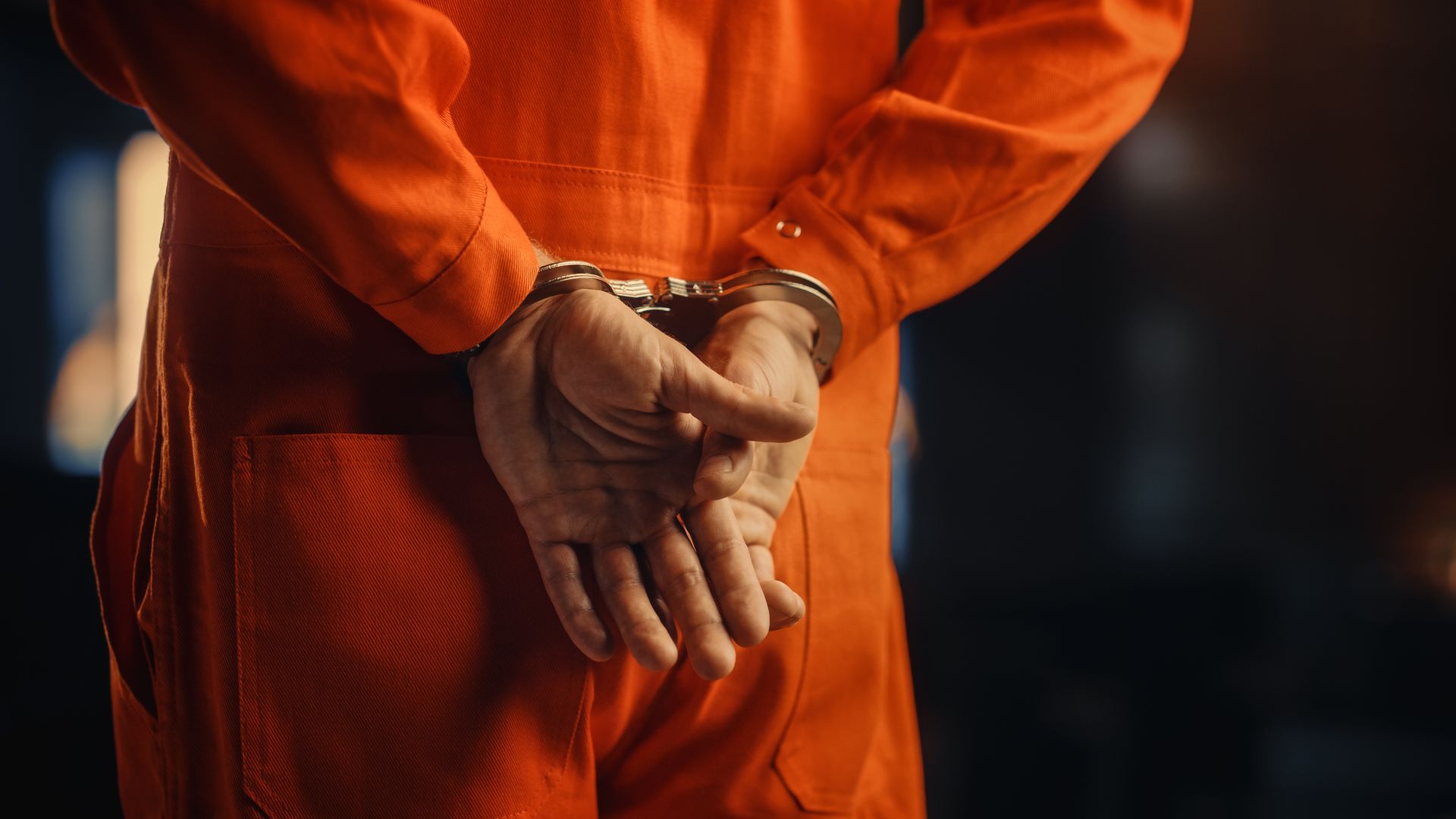 Person in an orange prison jumpsuit with handcuffed hands clasped behind their back