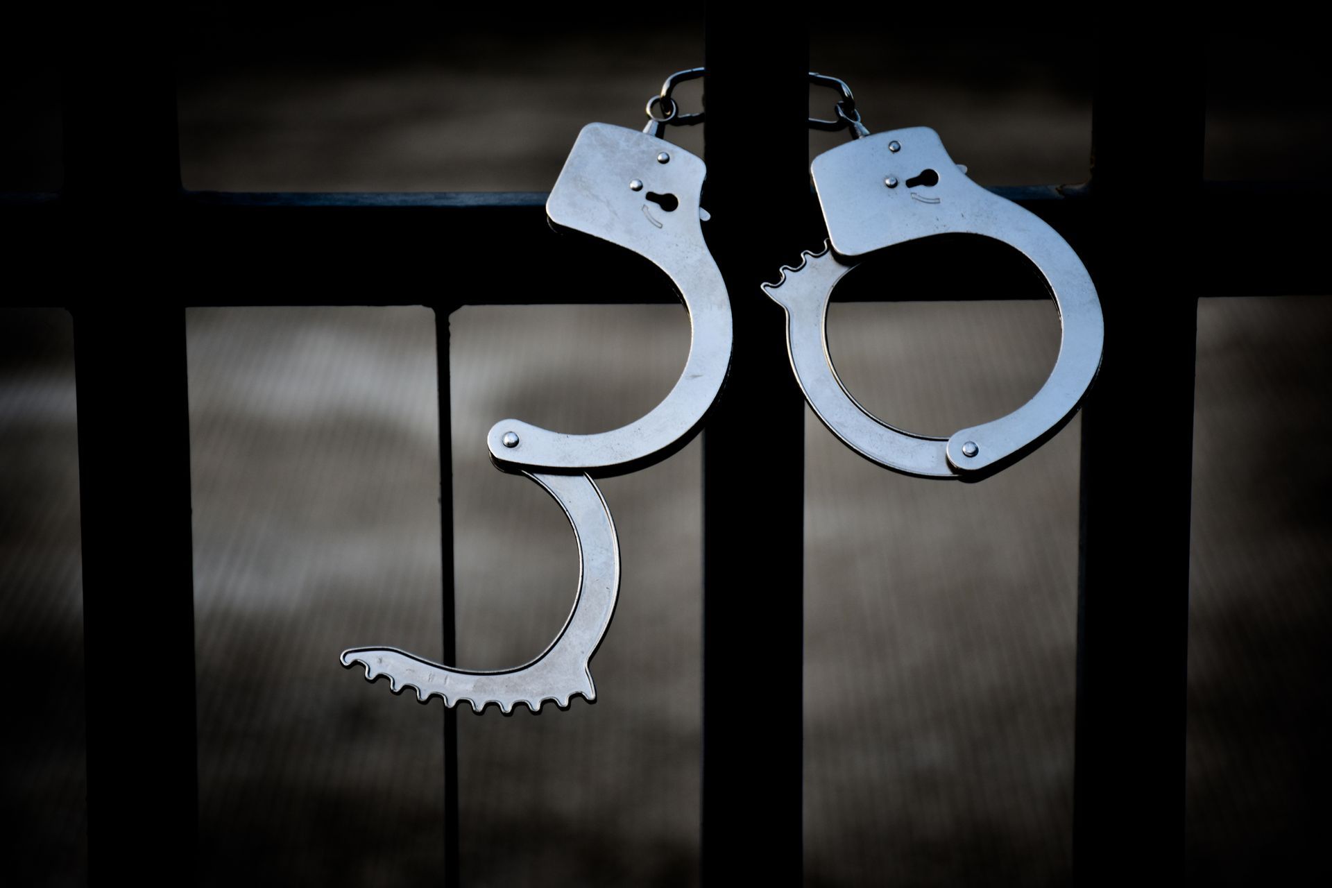 Open handcuffs hanging on a dark metal gate