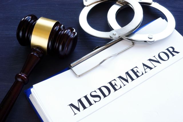Judge’s gavel and handcuffs beside a “MISDEMEANOR” document on a desk
