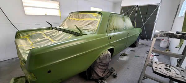 Green classic car in a workshop, masked for paint with wheels removed and tools nearby
