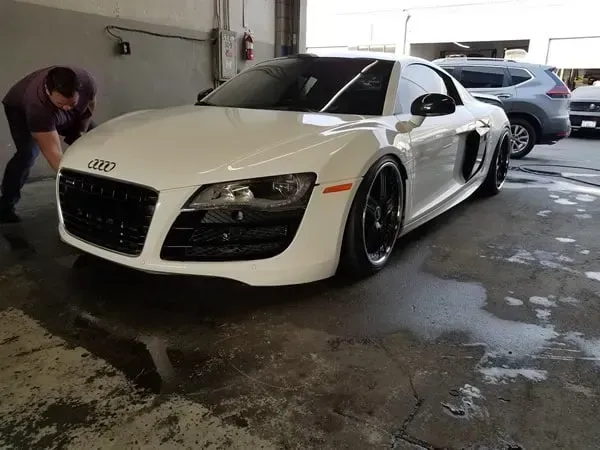 White Audi R8 parked in a garage, with a person cleaning it on the left.
