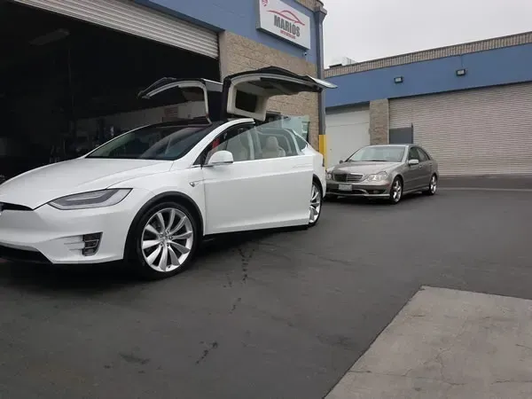 White Tesla with open rear hatch parked outside a building, with a gray sedan behind it