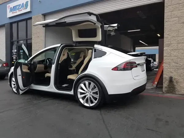 White Tesla Model X with falcon-wing doors open outside a garage bay