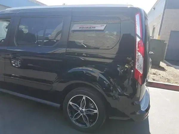 Black compact van parked outdoors in bright sunlight, side view with tinted windows and alloy wheels