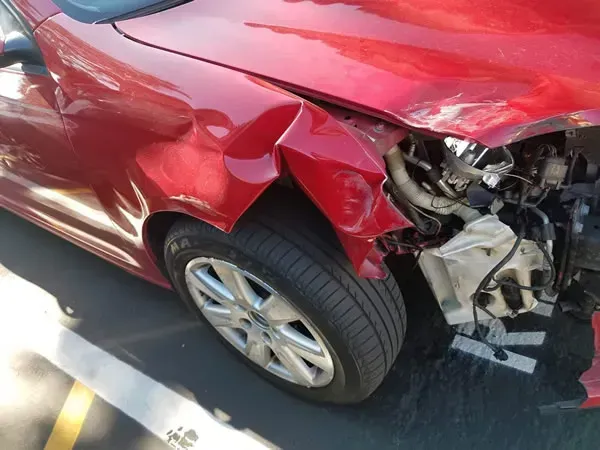 Red car with severe front-right collision damage, parked beside a curb.