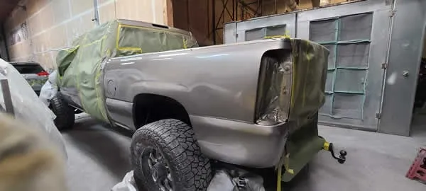 Gray pickup truck in a workshop, partially covered in green masking plastic during body repair.
