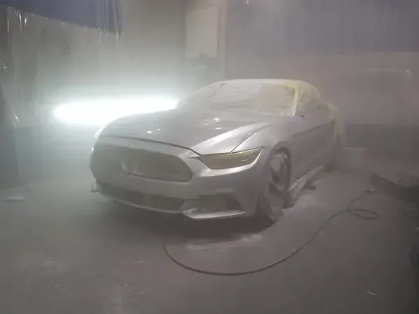 Silver sports car in a foggy, dim garage with bright lights behind it