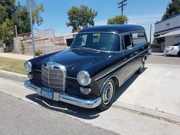 Dark blue vintage Mercedes sedan parked on a sunny street curb.
